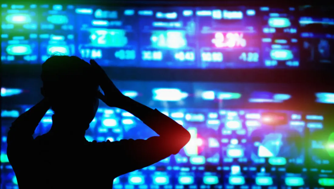 تصویر سایهنمای فردی که دستانش را روی سر گذاشته و به نمایشگر بازار سهام با اعداد منفی نگاه میکند.