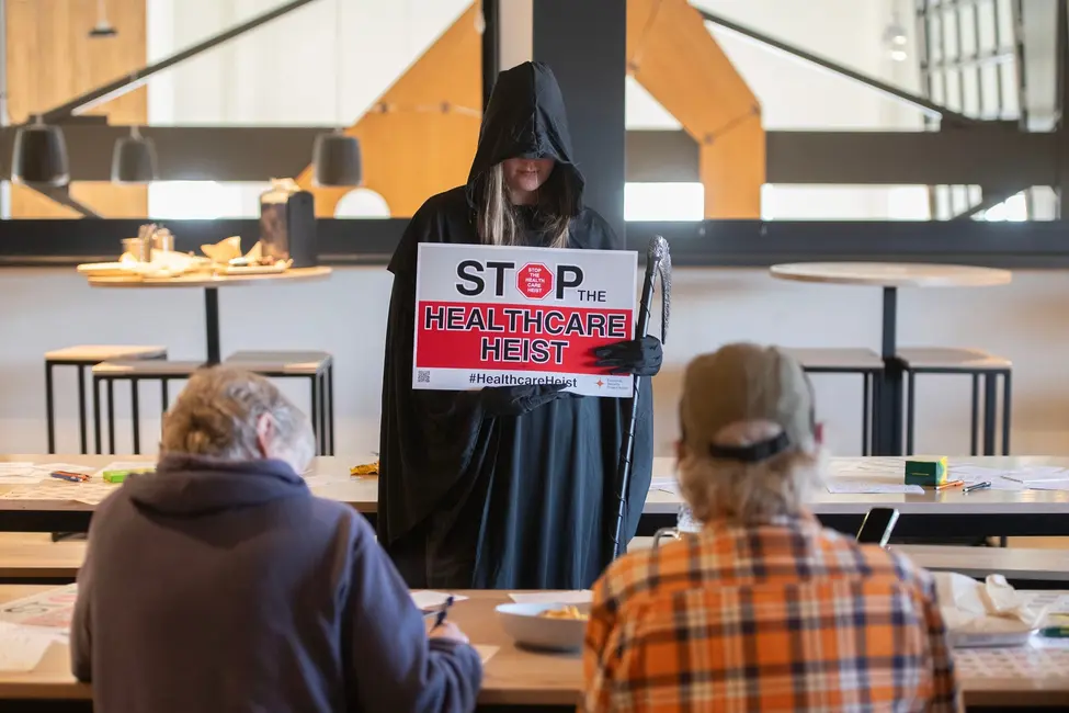 پریا تلنگ، با لباس فرشته مرگ، در اولین روز ثبتنام بیمه در نورتگلن، کلرادو، تابلویی در اعتراض به کاهش بودجه بهداشت و درمان در دست دارد، ۱ نوامبر ۲۰۲۵.