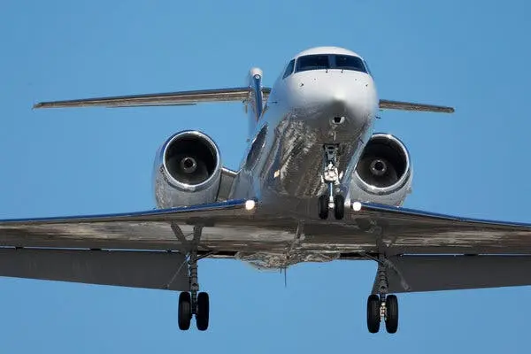 نمای نزدیک، یک هواپیمای جت به طور مستقیم به سمت دوربین در برابر آسمان آبی پرواز میکند.