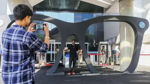 عکس بلومبرگ از گتی ایمیجز؛ یک شرکت‌کننده برای عکاسی با یک عینک بزرگ پس از مراسم لیست‌کردن لنس‌کارت در بورس ملی (NSE) ممبای، هند، روز دوشنبه ۱۰ نوامبر ۲۰۲۵.