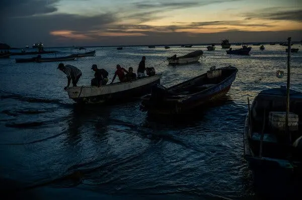 قایق‌های کوچک در آب‌های کم‌عمق با مردانی داخل یکی از آن‌ها.