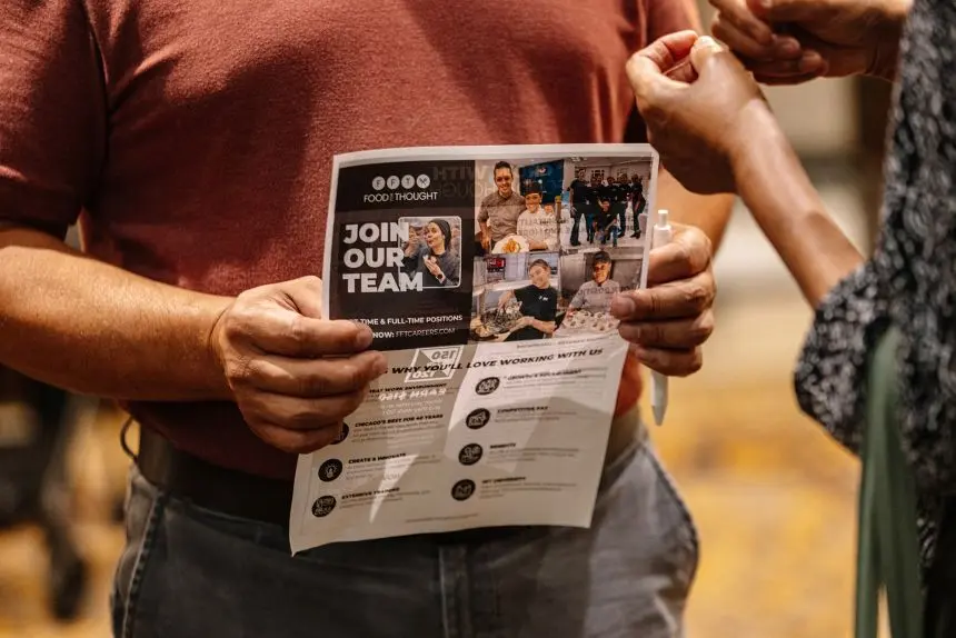 یک شرکت‌کننده برگه‌ای با متن "به تیم ما بپیوندید" را در نمایشگاه شغلی Best Hire Chicago در تاریخ ۷ آگوست در دست دارد.