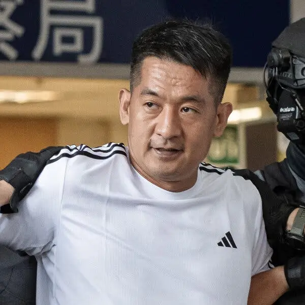 مردی با تیشرت سفید که توسط افسران مسلح همراهی میشود.