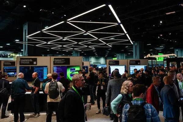 افراد ایستاده در میان نمایشگاههای دیجیتال و صفحهنمایشها؛ یک چراغ نورثلاثی بالای سرشان.