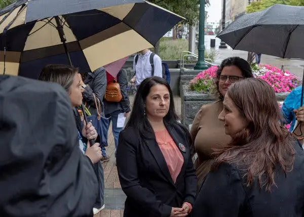 اتل هاکسیاج در میان گروهی از افراد با چتری ایستاده است. او بهنظر متفکر میآید.