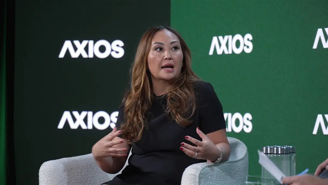 امیلی چوئی، مدیر عملیاتی Coinbase، در مقابل پس‌زمینهٔ لوگوی "Axios" صحبت می‌کند.