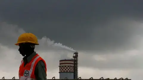 تصویر Getty Images: کارگری در مقابل یک کارخانه شیمیایی که دود خروجی را به هوای مومبای، هند، در دوشنبه ۱۳ سپتامبر ۲۰۱۰ منتشر میکند.