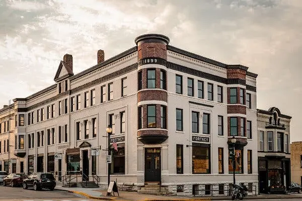 یک ساختمان سه طبقه در نبش یک خیابان قرار دارد. بالای دو پنجره آن کلمه «FORTNEY» و نزدیک به بالای نبش ساختمان عدد «۱۸۹۹» دیده می‌شود.