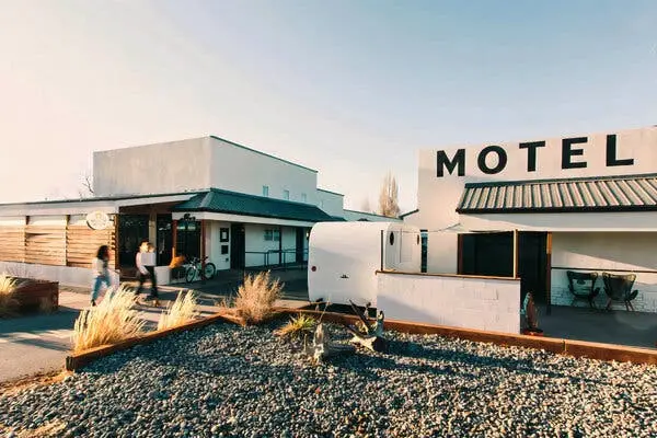 دو نفر که کمی تار دیده می‌شوند، بین دو ساختمان سفید در حال راه رفتن هستند. روی یکی از ساختمان‌ها کلمه «MOTEL» به چشم می‌خورد.