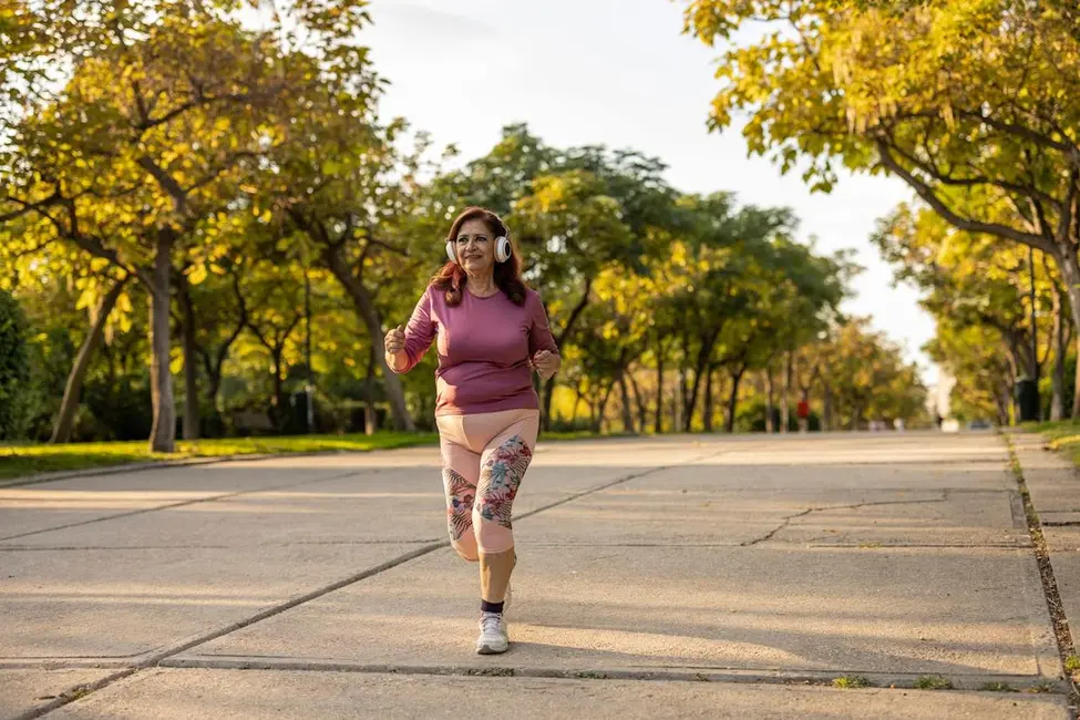 زن سالخورده با اندام توپر که با هدفون بی‌سیم در پارک عمومی در حال دویدن است