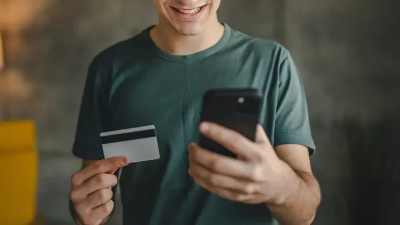 مرد جوانی که در یک دست کارت اعتباری و در دست دیگر گوشی موبایل دارد