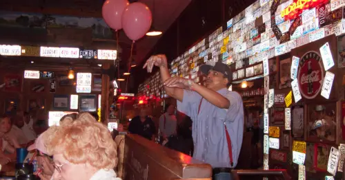 مردی با پیراهن راهراه آبی و سفید، سوسپندِرهای قرمز و کلاه آبی، یک رول نان را از یک طرف سالن غذاخوری به سمت دیگر در کافه لمبرت میپرتابید.