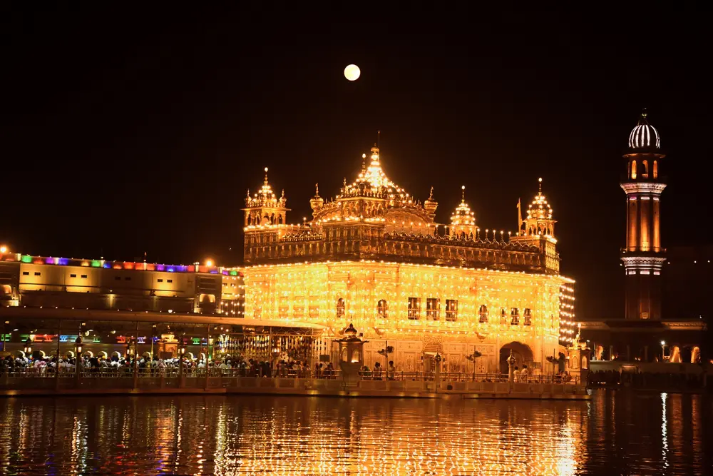 اَبَرماه در پشت معبد طلایی نورانی طلوع می‌کند، در حالی که پیروان آیین سیک برای گرامیداشت سالروز تولد اولین پیشوای خود، گورو نانک، در امریتسار، هند، در روز چهارشنبه، ۵ نوامبر ۲۰۲۵، دعا می‌کنند. (عکس: پرابجوت گیل/آسوشیتدپرس)