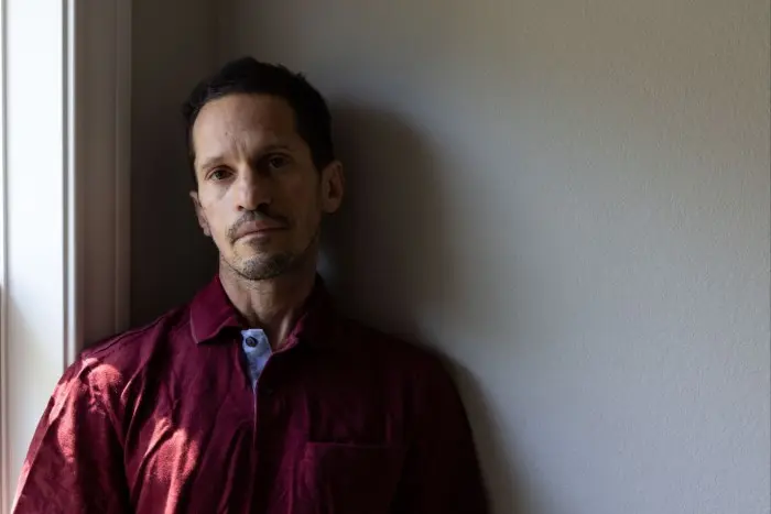 مردی با ظاهر جدی و موهای کوتاه تیره در ژاکت کاری قرمز