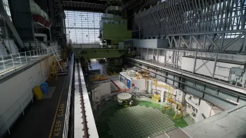 بخش بالایی یک رآکتور هسته‌ای دایره‌ای در پیش‌زمینه؛ در حالی که سالن توربین به سمت دوردست کشیده شده است.