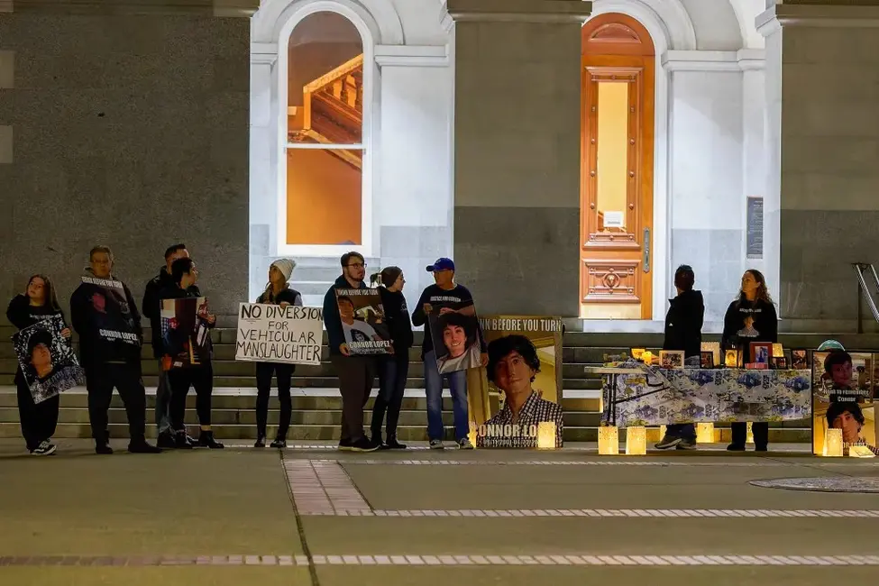 نمای گسترده‌ای از افرادی که جلوی یک ساختمان ایستاده‌اند و تابلوها و عکس‌های افرادی که به‌دست رانندگان مست کشته شده‌اند را در دست دارند. یک نفر یک تابلو می‌گیرد که نوشته شده «بدون انحراف برای قتل غیرقابل‌قانونی وسیله نقلیه».