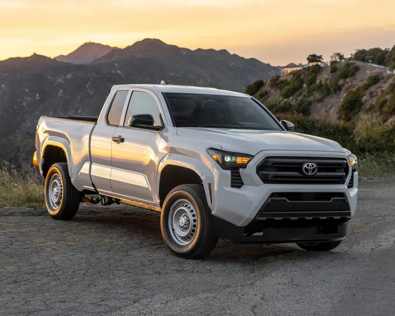 شاحنه سفید تویوتا با جبهه سیاه و چرخ‌های فولادی، پارک شده بر روی جاده‌ای کوهستانی در غروب خورشید