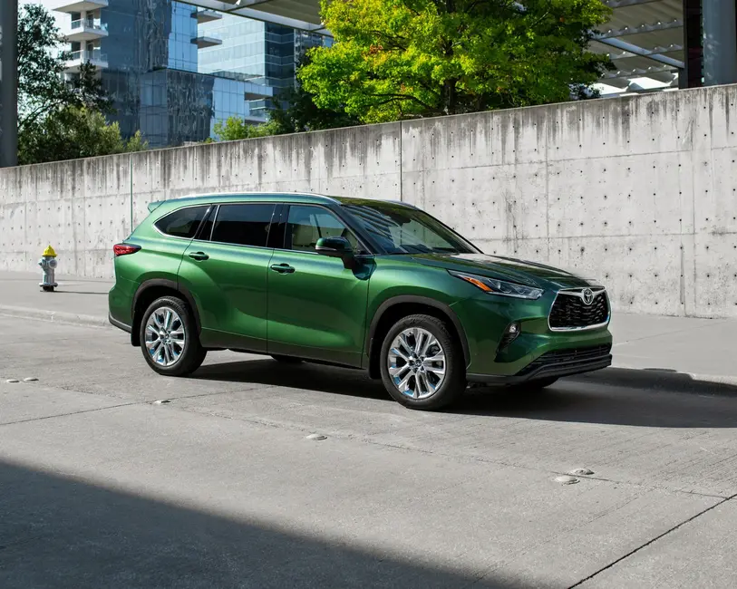 SUV سبز تویوتا پارک شده بر روی خیابان شهری با دیوار بتنی و ساختمان‌های مدرن در پس‌زمینه