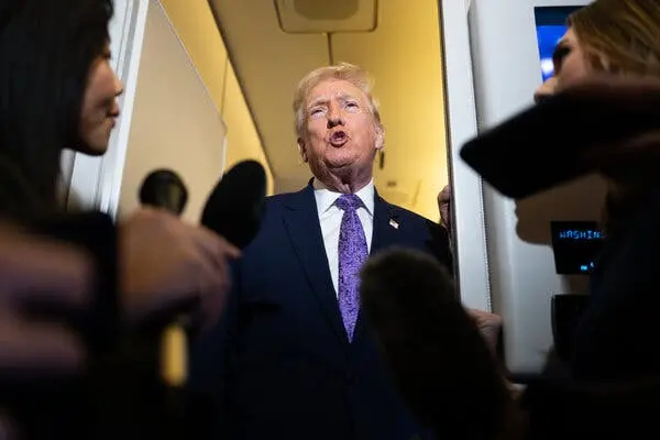 رئیس‌جمهور ترامپ در هواپیمای اف‌ن‌وان سخن می‌گوید و خبرنگاران با میکروفن‌ها در پیش‌زمینه حضور دارند.